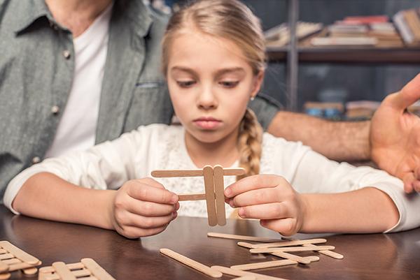 young girl building with popsicle sticks
